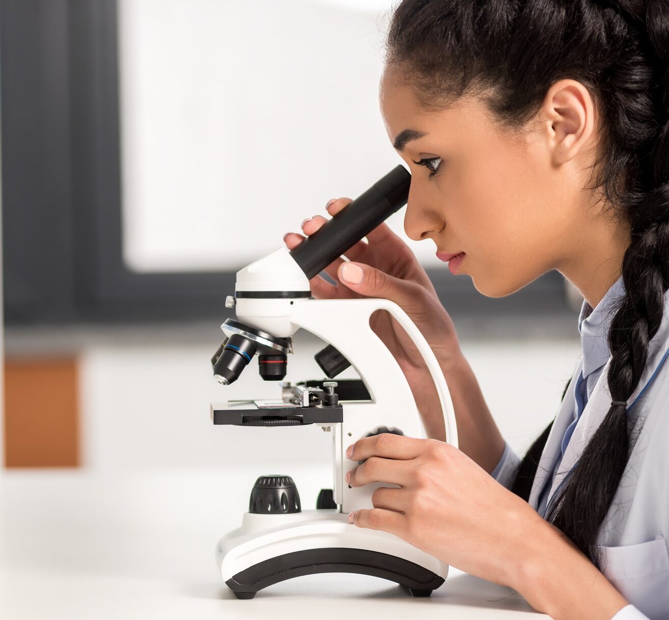 Side view of young scientist in lab coat working with microscope in laboratory